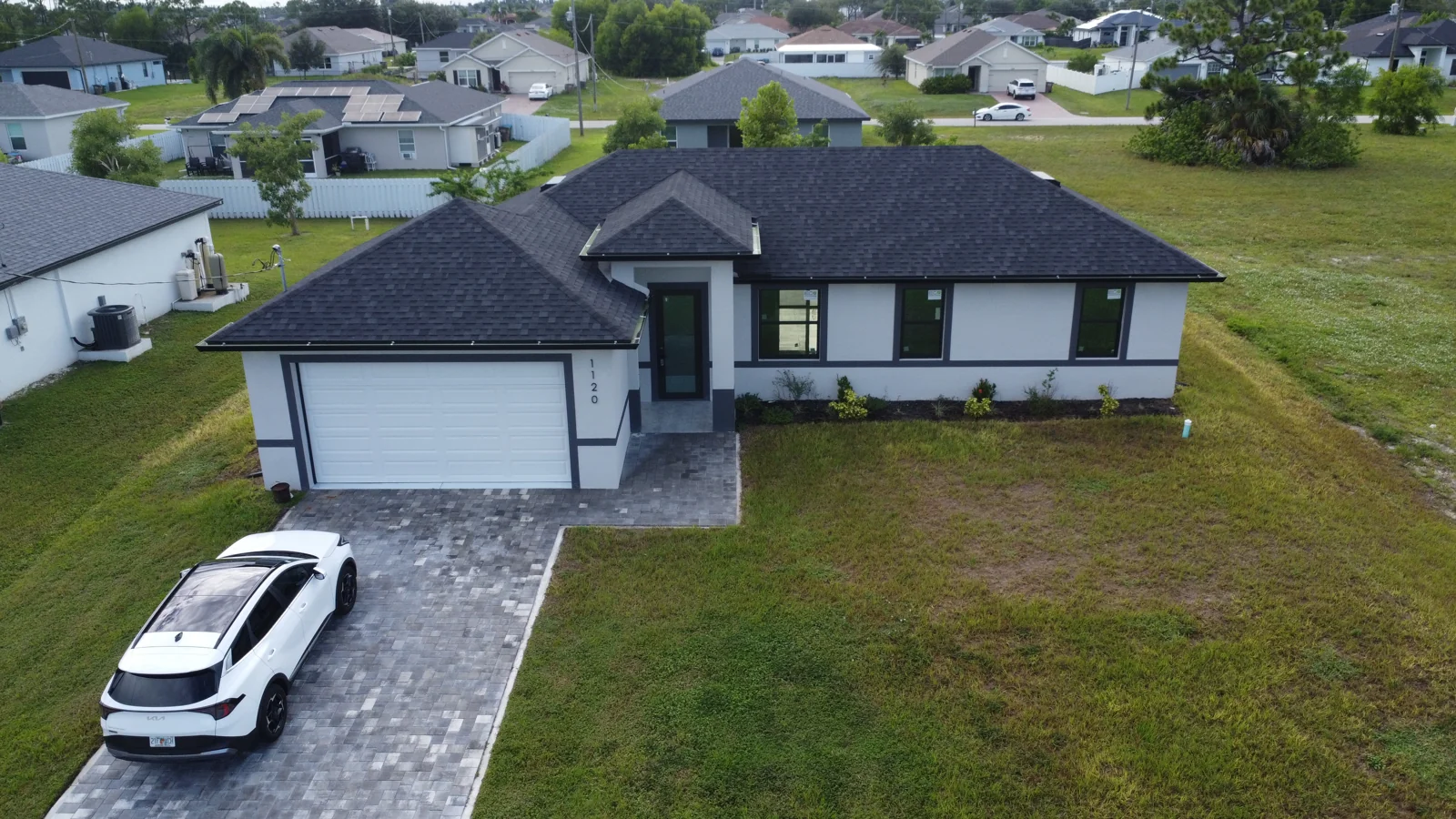 Aerial view of a single-story home with a dark roof and paved driveway