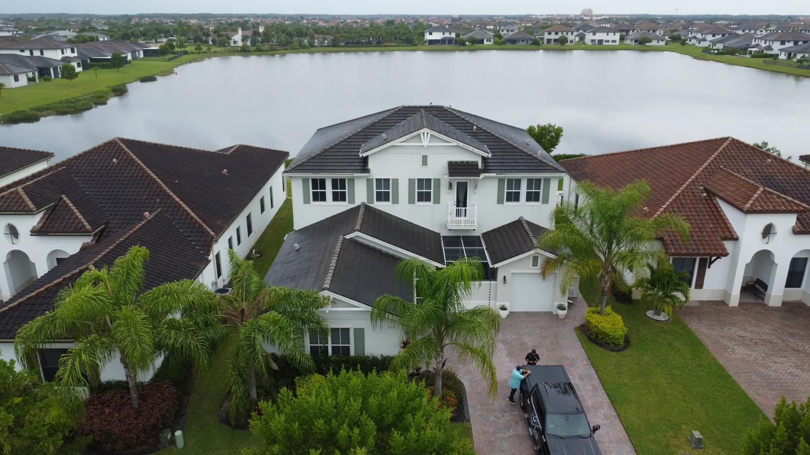 Aerial view of a waterfront home with a tile roof and palm-lined driveway
